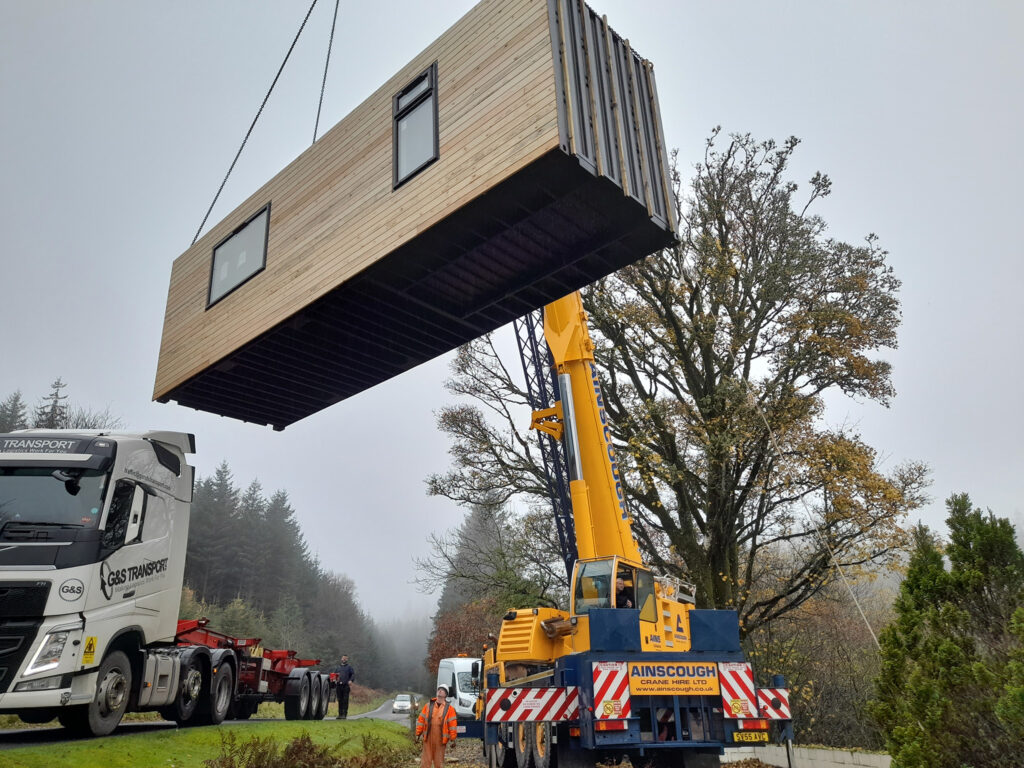 Cottagein the woods crane lifting converted shipping container modular building into position on-site