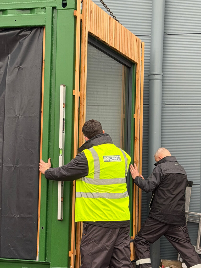 InBox Projects staff installing contaner canteen space on-site hi-vis branded vest timber clad green container
